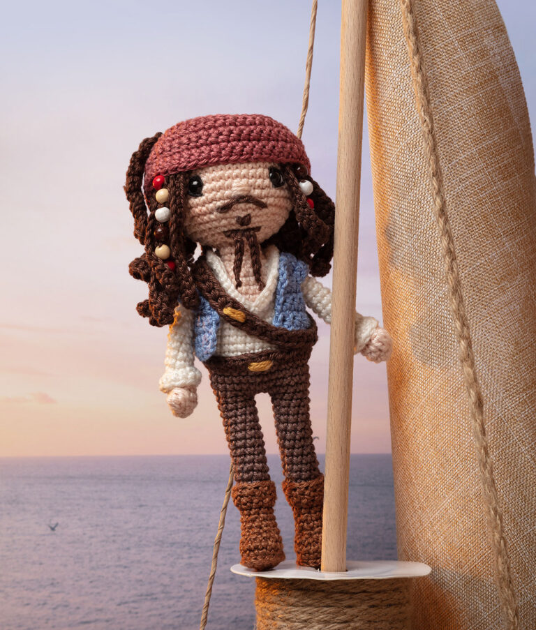 inszeniertes Foto einer Jack Sparrow Häkelpuppe stehend auf einem Segelmast vor einem Abendhimmel für ein Promi-Häkelbuch