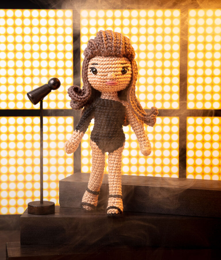 inszeniertes Foto einer Beyoncé Häkelpuppe auf einer Bühne mit Mikrophon und LED Panels für ein Promi-Häkelbuch