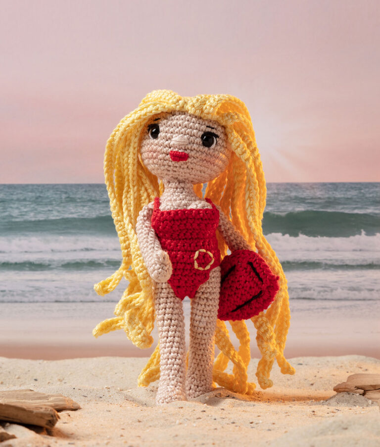 inszeniertes Foto einer Pamela Anderson Häkelpuppe aus dem Film Baywatch mit Retterboje am Strand für ein Promi-Häkelbuch