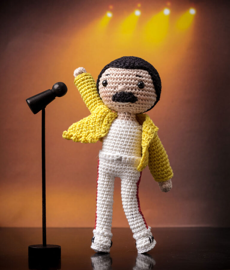 inszeniertes Foto einer Freddy Mercury Häkelpuppe auf der Bühne mit Mikrophon und Bühnenbeleuchtung für ein Promi-Häkelbuch
