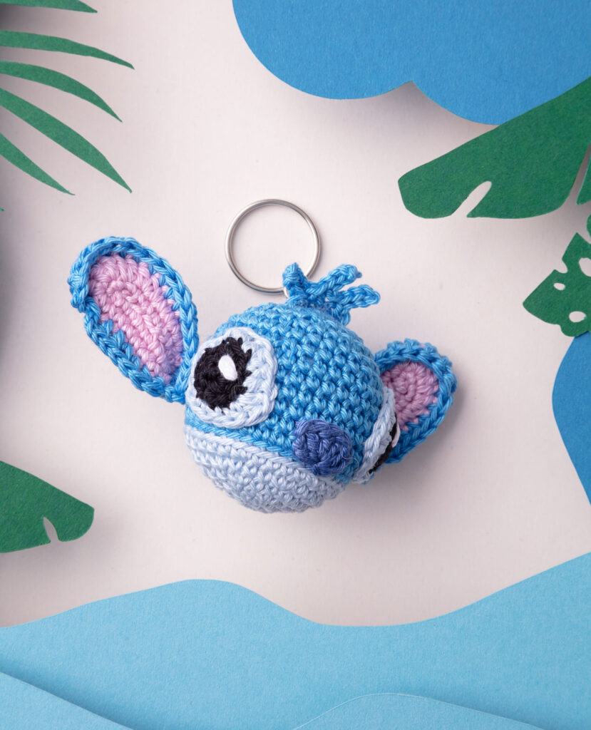 Produktfoto eines DIY gehäkelten Stich aus Lio und Stich als Schlüsselanhänger in einer Paper-Art-Kulisse mit Urwald, Wolken und Wasser