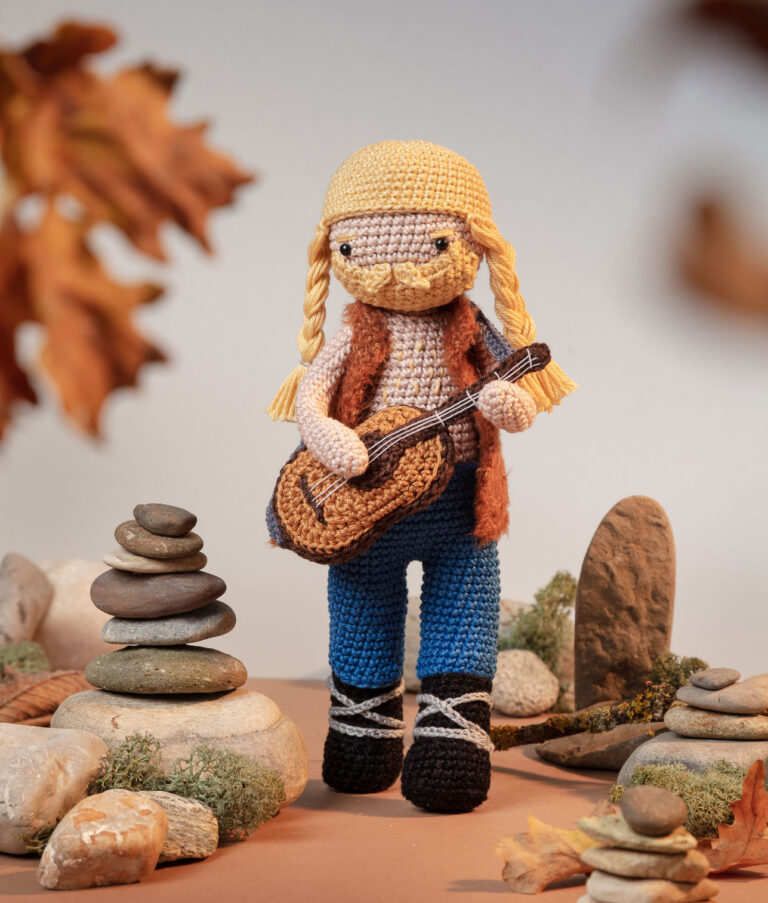Produktfoto einer Wikinger-Häkelpuppe in einem aufwendigen Setting das eine nordisch herbstliche Landschaft zeigt, dekoriert mit echten Naturmaterialien wie Zweige, Moos und Steine