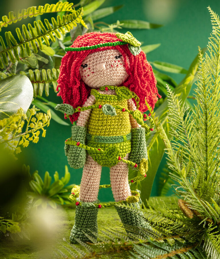 Produktfoto einer Häkelpuppe verkleidet als starke Superheldin in einem aufwendigen Setting das einen wilden Dschungel zeigt, dekoriert mit vielen Pflanzen, Moss und Zweigen