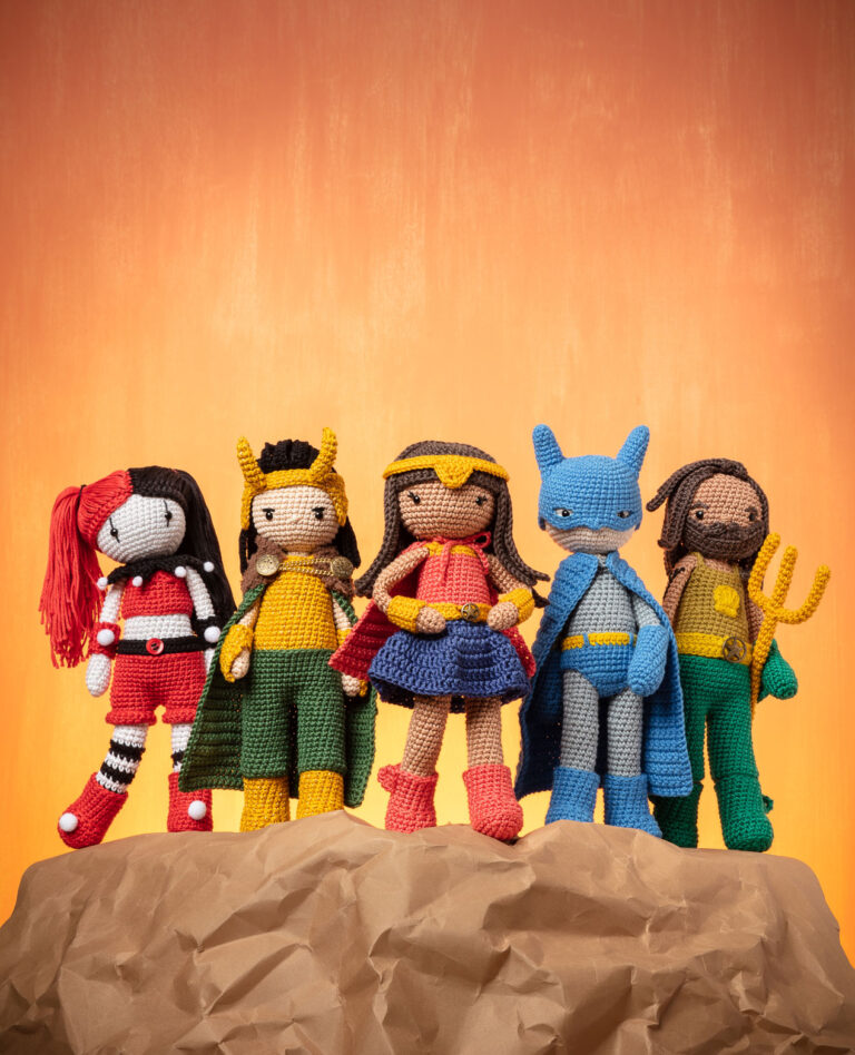 Titelbild für die Fotoproduktion eines Häkelbuchs für Superhelden das fünf verschiedene Häkelpuppen stehend auf einem Felsen vor einem flammenden Hintergrund zeigt