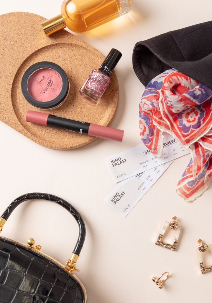 Imagefoto zum Thema "Me-Time" für Frauen das ein Arrangement mit einer schwarzen Handtasche, Schmuck, Make-up und Kinotickets zeigt