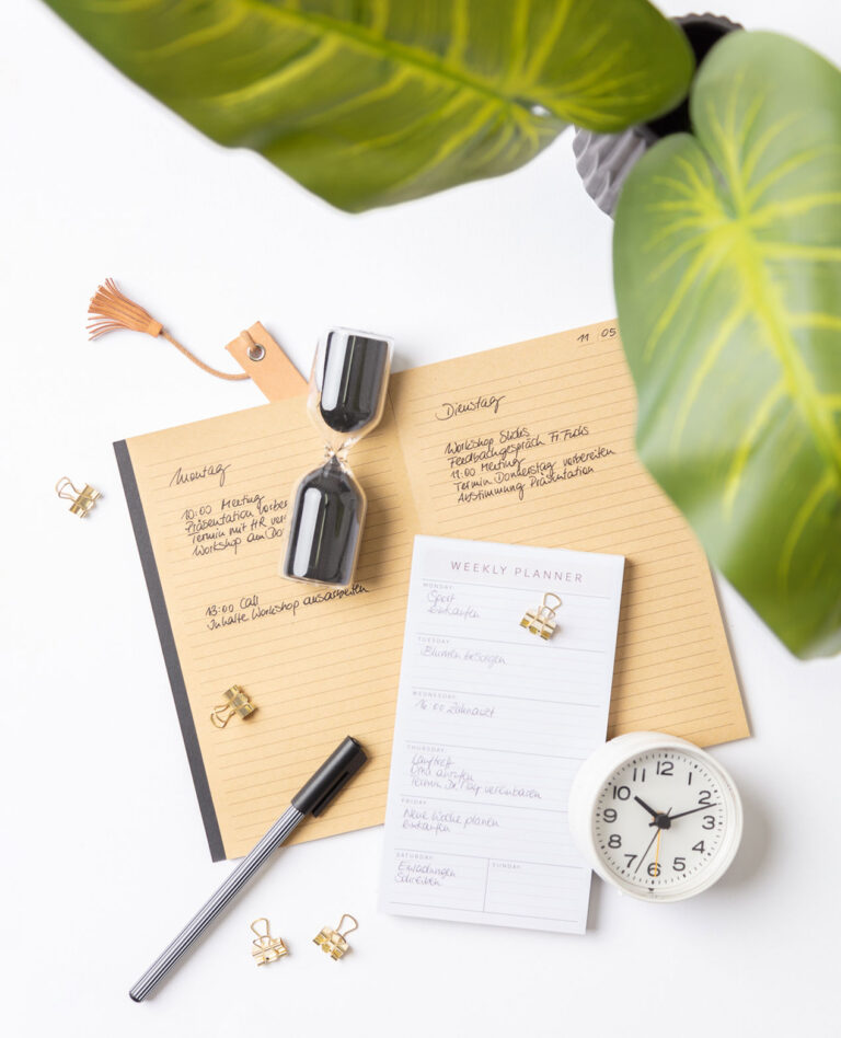 Titelfoto für die Fotoproduktion eines Ratgebers, das einen Wochenplaner, ein Notizbuch mit täglichen To-Dos, eine Pflanze, eine Sanduhr und einen Wecker zeigt