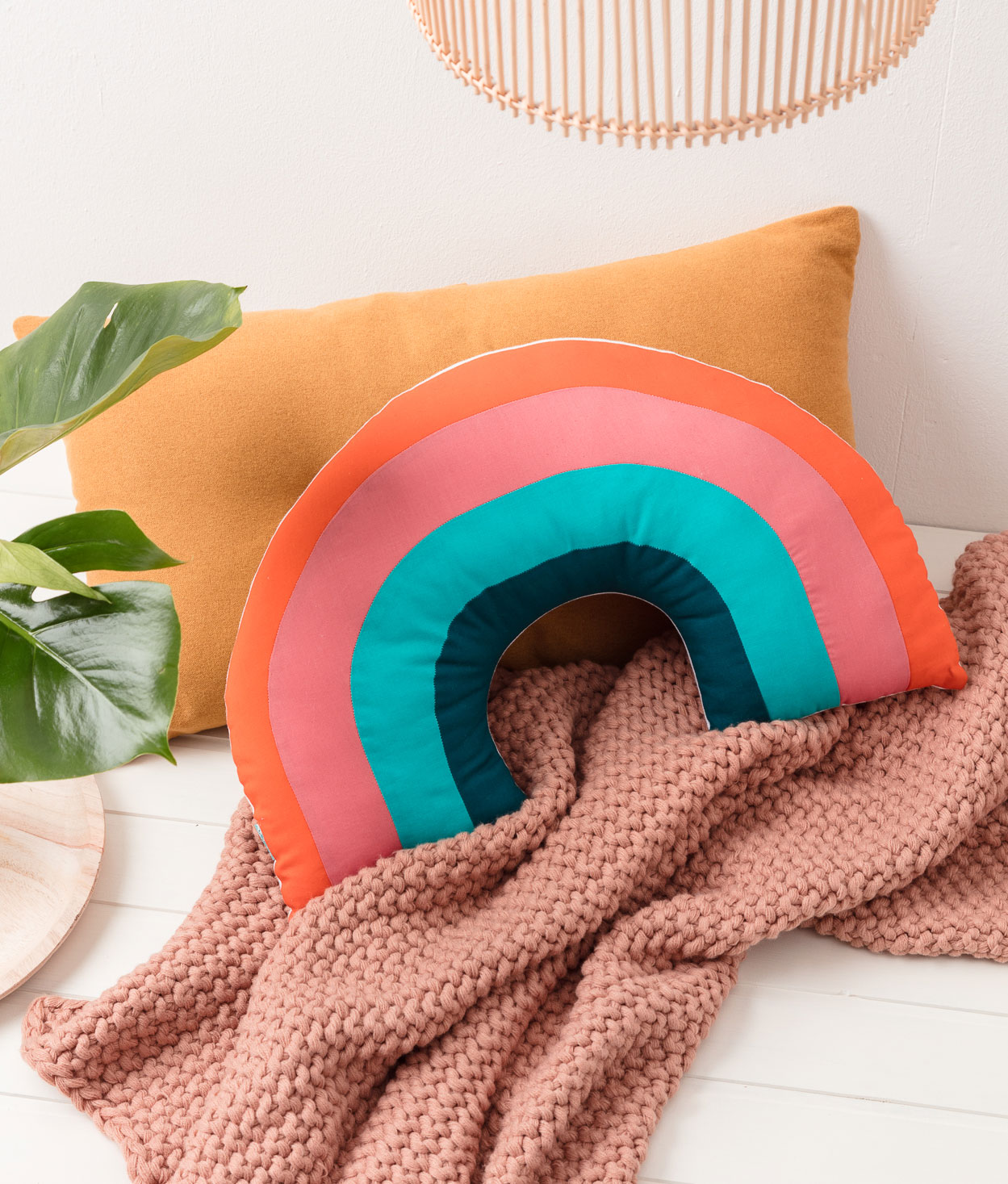 Produktfoto eines selbstgenähten Regenbogen-Kissens in einer Interior-Kulisse mit Kissen, Pflanzen und einer weichen Decke