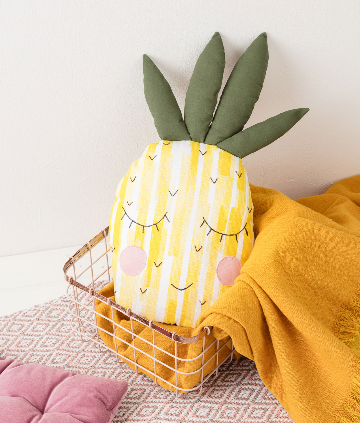 Produktfoto eines selbstgenähten Ananas-Kissens in einem Körbchen in einer Interior-Kulisse mit Kissen, Teppich und einer gelben Decke