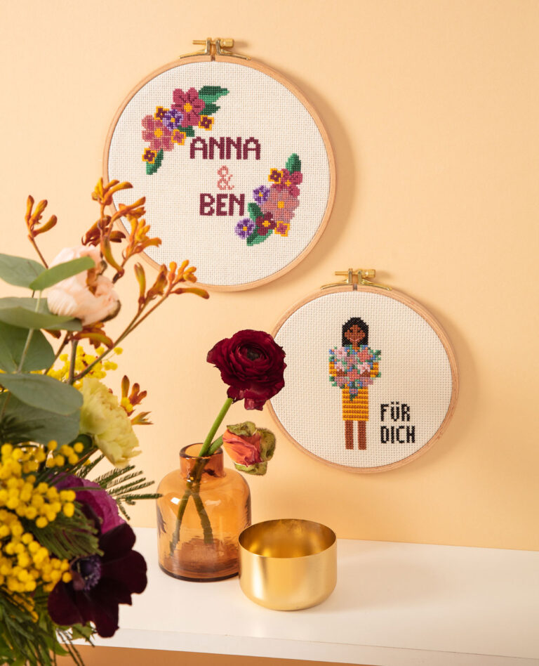 Titelfoto für die Fotoproduktion eines Stickbuchs das zwei bestickten Stickrahmen an der Wand, Blumen und Vasen auf einem Regalbrett zeigt