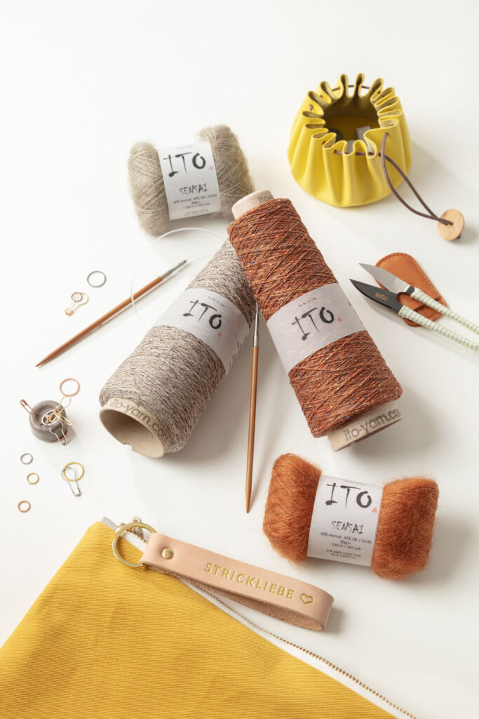 Produktfoto zum Thema Stricken mit mehreren KNäuel und Konen der Firma ITO, Stricknadeln und weiteren Strickutensilien in den Farben gelb, orange, taupe
