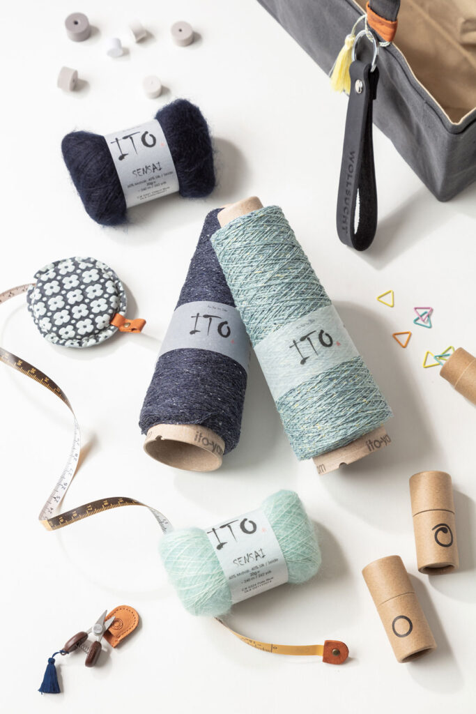 Produktfoto zum Thema Stricken mit mehreren Knäuel und Konen der Firma ITO, Stricknadeln und weiteren Strickutensilien in den Farben blau, türkis und braun