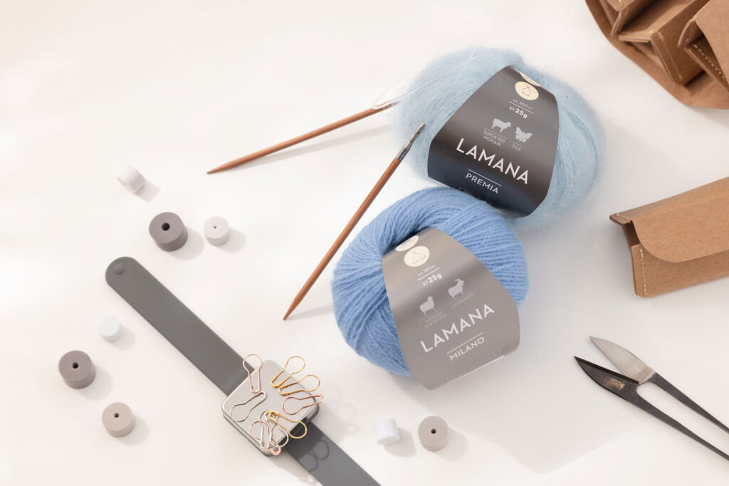 Produktfoto eines schönen Arrangements zum Thema Stricken mit zwei blauen Wollknäuel von Lamana und verschiedenem Strickzubehör
