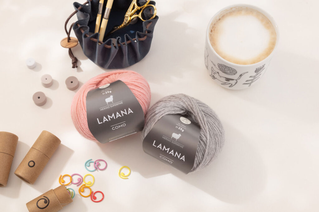 Produktfoto eines schönen Arrangements zum Thema Stricken mit zwei Wollknäuel von Lamana, einer Kaffeetasse und verschiedenem Strickzubehör