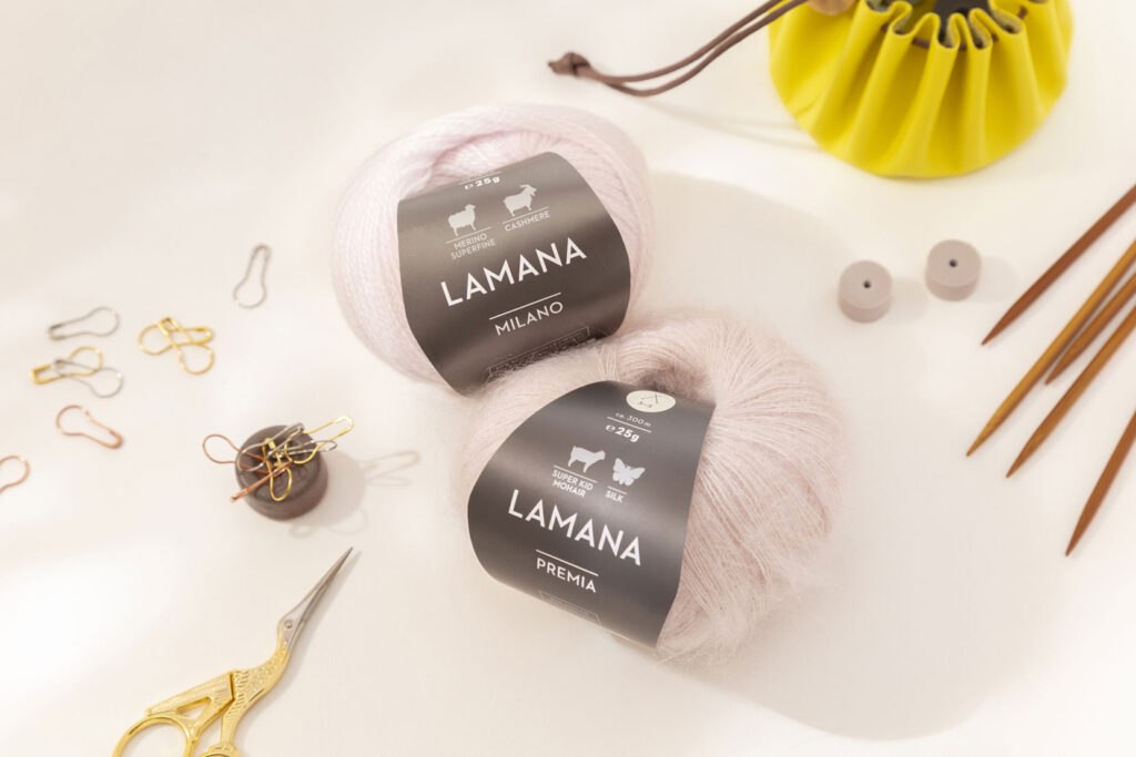 Produktfoto eines schönen Arrangements zum Thema Stricken mit zwei rosanen Wollknäuel von Lamana und verschiedenem Strickzubehör