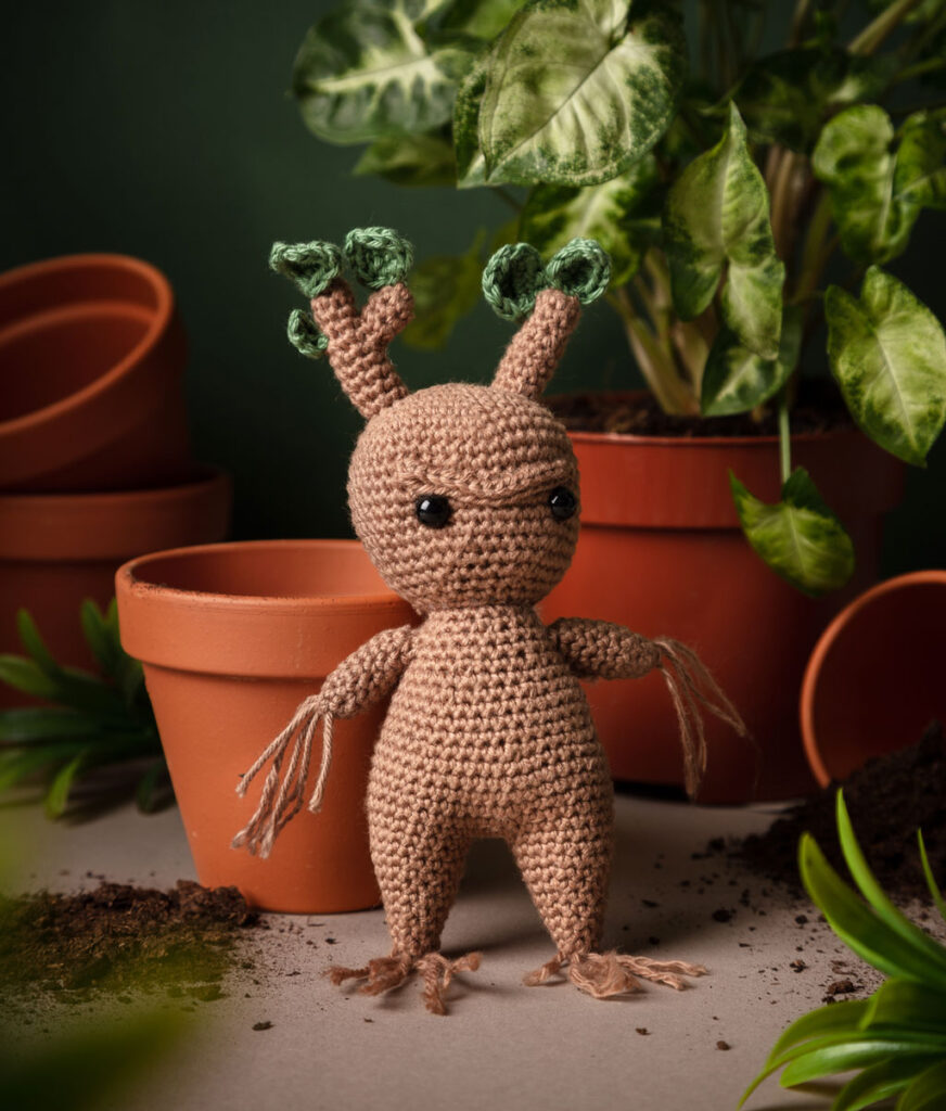 Produktfoto einer Alraune-Häkelfigur aus Harry Potter in nachgestellter Mini-Kulisse mit Pflanzen, Blumentöpfen und Erde