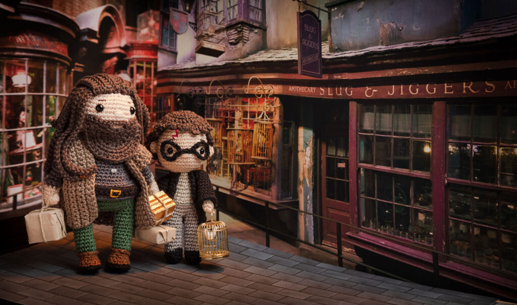 Produktfoto von zwei Häkelfiguren aus Harry Potter - Hagrid & Harry Potter - mit Einkäufen im Arm in nachgestellter Mini-Kulisse der Winkelgasse