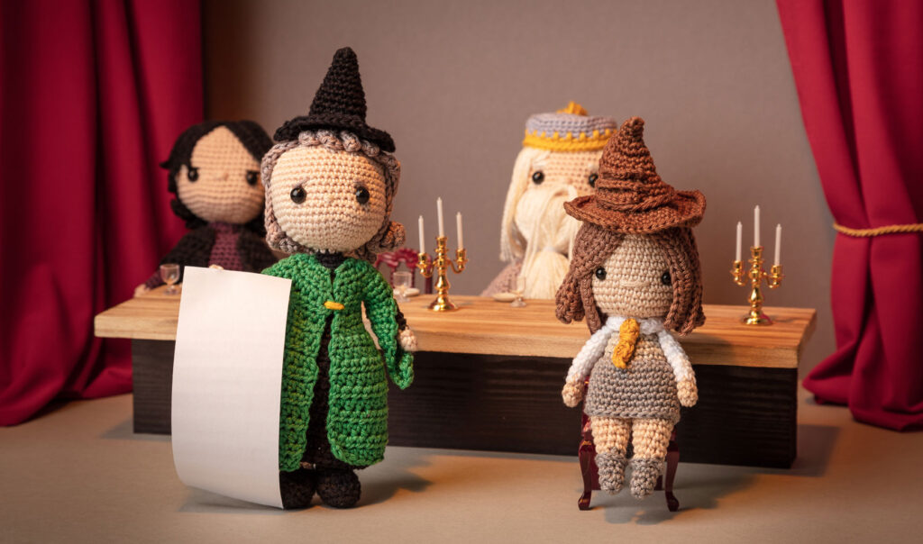 Produktfoto von vier Häkelfiguren aus Harry Potter - Snape, Dumbledore, McGonagall & Hermine - in nachgestellter Mini-Kulisse des Speisesaals mit Esstisch und dem sprechenden Hut