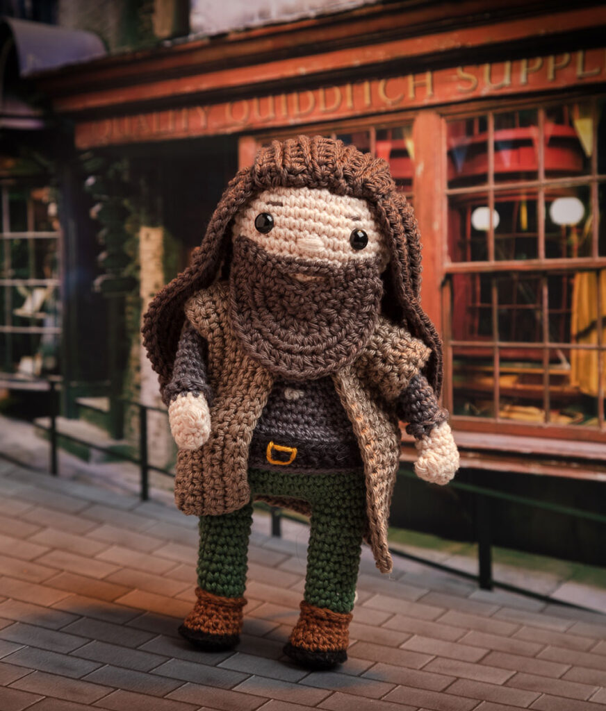 Produktfoto einer Hagrid-Häkelfigur aus Harry Potter in nachgestellter Mini-Kulisse der Winkelgasse
