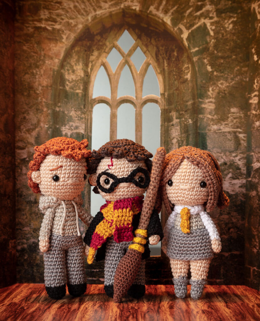 Titelfoto von drei Häkelfiguren aus Harry Potter - Ron, Harry Potter & Hermine - in nachgestellter Mini-Kulisse eines Raumes in Hogwarts