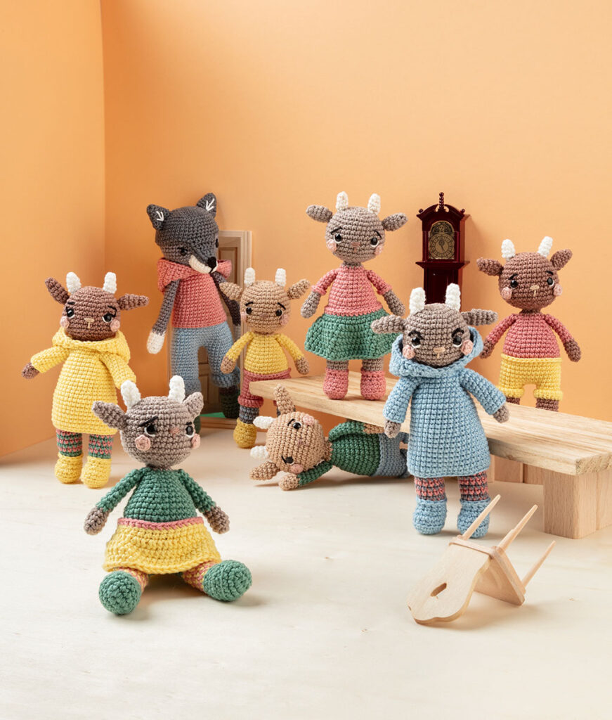 Produktfoto von einem Wolf und sieben Geißlein als moderne Häkelfiguren in einer Zimmer-Kulisse aus Papier dekoriert mit Tisch, Stühlen und einer Standuhr