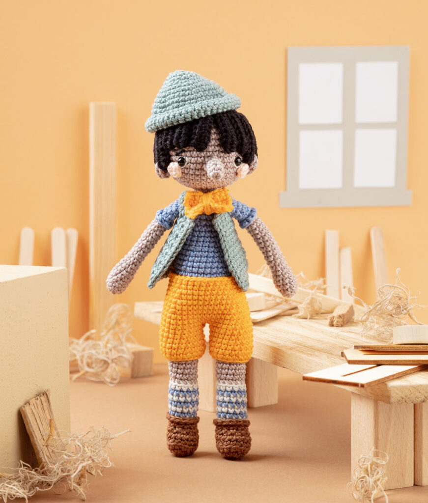 Produktfoto von Pinocchio als moderne Häkelfigur in einer hellen Kulisse einer Werkstatt dekoriert mit Holz und Spänen