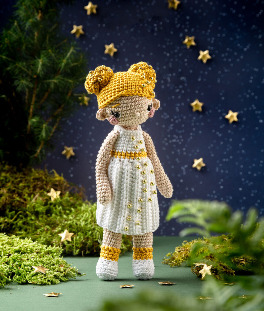 Produktfoto einer modern gestalteten Häkelfigur des Sterntalers in einer dunklen Kulisse aus Papier dekoriert mit Zweigen, Moos und goldenen Sternen