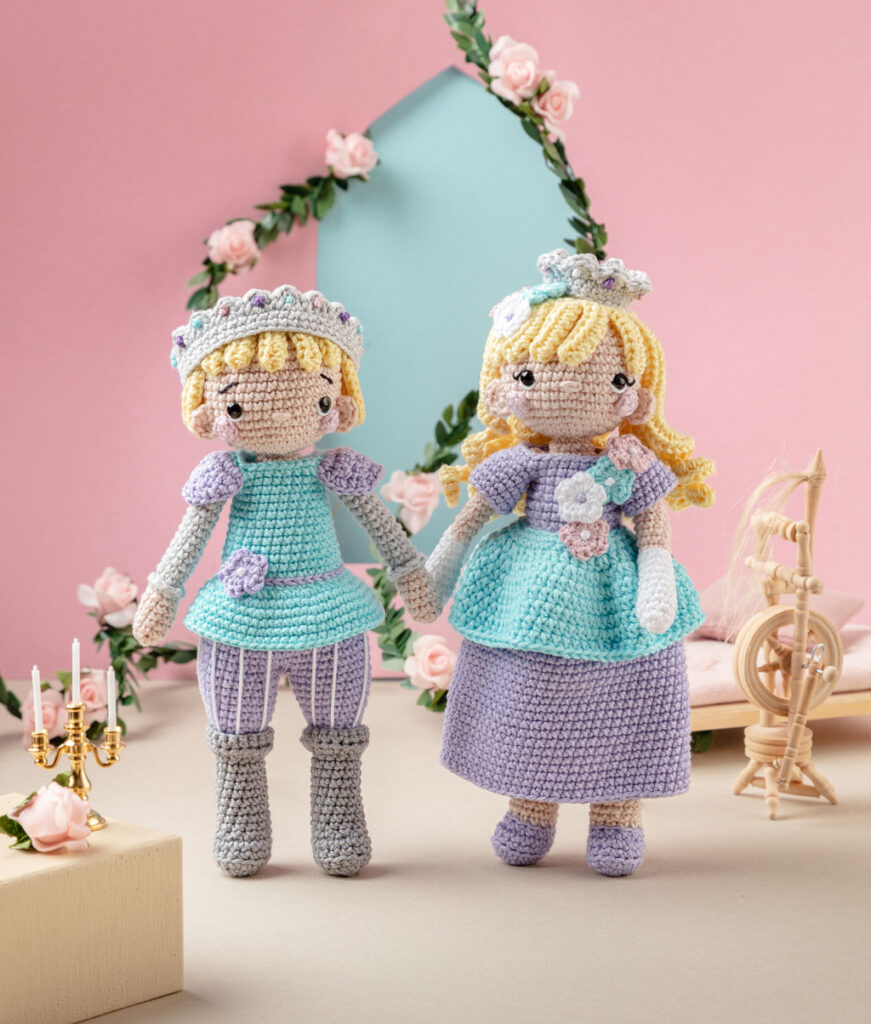 Produktfoto von zwei modern gestalteten Häkelfiguren aus Dornröschen in einer märchenhaften Kulisse dekoriert mit Rosenranken, Spinnrad und Kerzenleuchtern