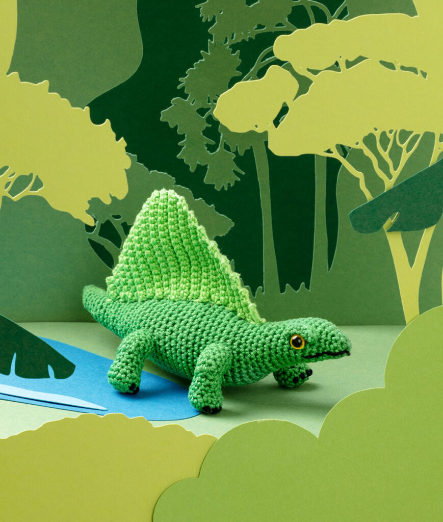 Produktfoto eines grünen Dinosauriers in grüner Paper-Art Kulisse mit verschiedenen Ebenen, die eine Landschaft der Urzeit ergeben