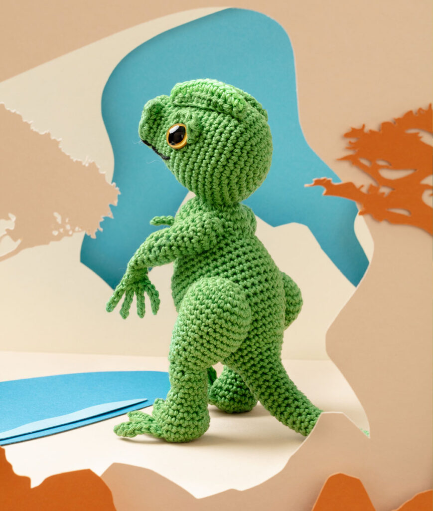 Produktfoto eines grünen Dinosauriers in beiger Paper-Art Kulisse mit verschiedenen Ebenen, die eine Landschaft der Urzeit ergeben