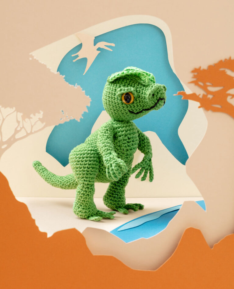 Titelfoto eines grünen Dinosauriers in Paper-Art Kulisse mit verschiedenen Ebenen die eine Landschaft der Urzeit ergeben