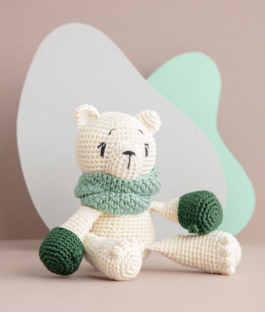 inszeniertes Produktfoto einer bekleideten Eisbären-Häkelpuppe vor einem Paper-Art Hintergrund mit verschiedenfarbigen runden, organischen Formen für ein Häkelbuch