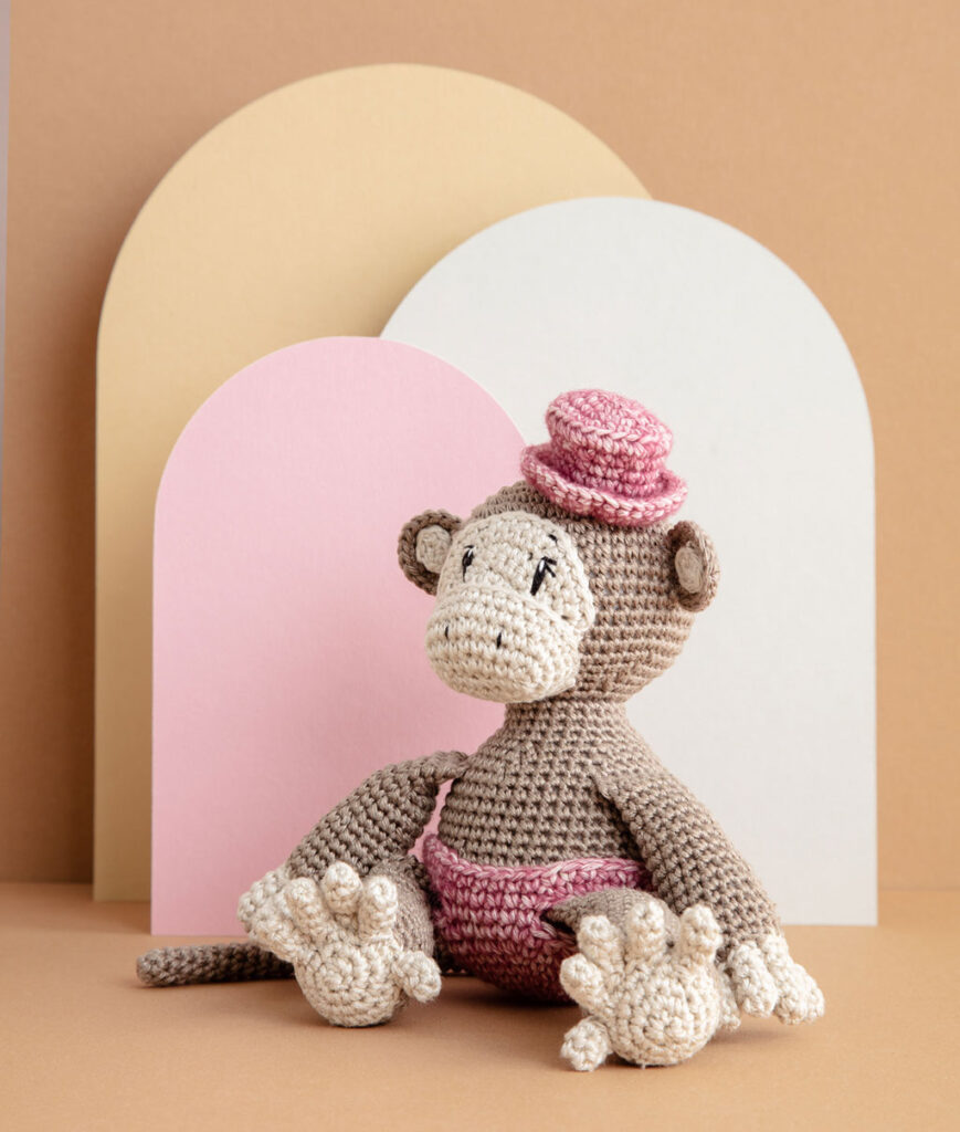 inszeniertes Produktfoto einer bekleideten Affen-Häkelpuppe vor einem Paper-Art Hintergrund mit verschiedenfarbigen runden, organischen Formen für ein Häkelbuch