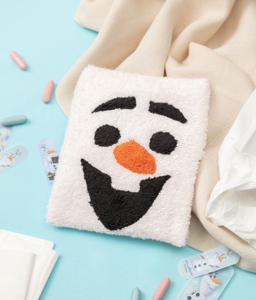 Produktfoto eines genähten Kühlpacks als Olaf-Figur auf blauem Hintergrund dekoriert mit Pflastern, Taschentüchern und einem Tuch für ein Kinder Nähbuch
