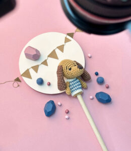 Making-of-Foto aus einem Fotoshooting, das eine gehäkelte Fingerpuppe als Dackel in einer Foto-Kulisse aus Papier und Holzkugeln zeigt