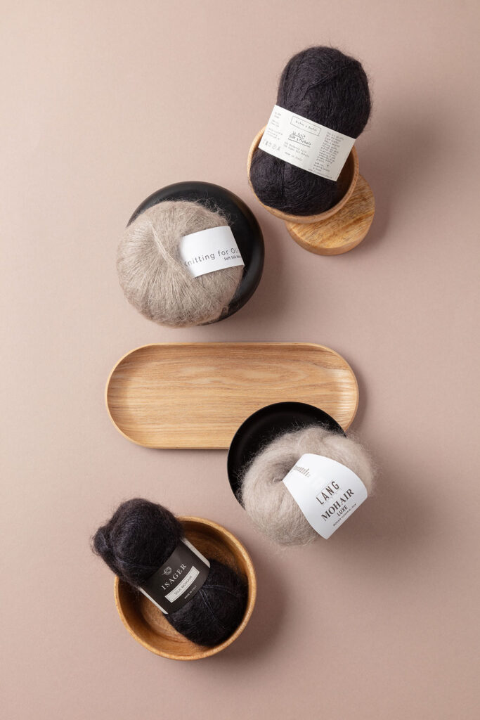 Arrangiertes Flatlay-Produktfoto auf braunem Untergrund, das vier unterschiedliche Knäuel Mohair-Wolle zeigt, die in verschiedenen Schalen liegen