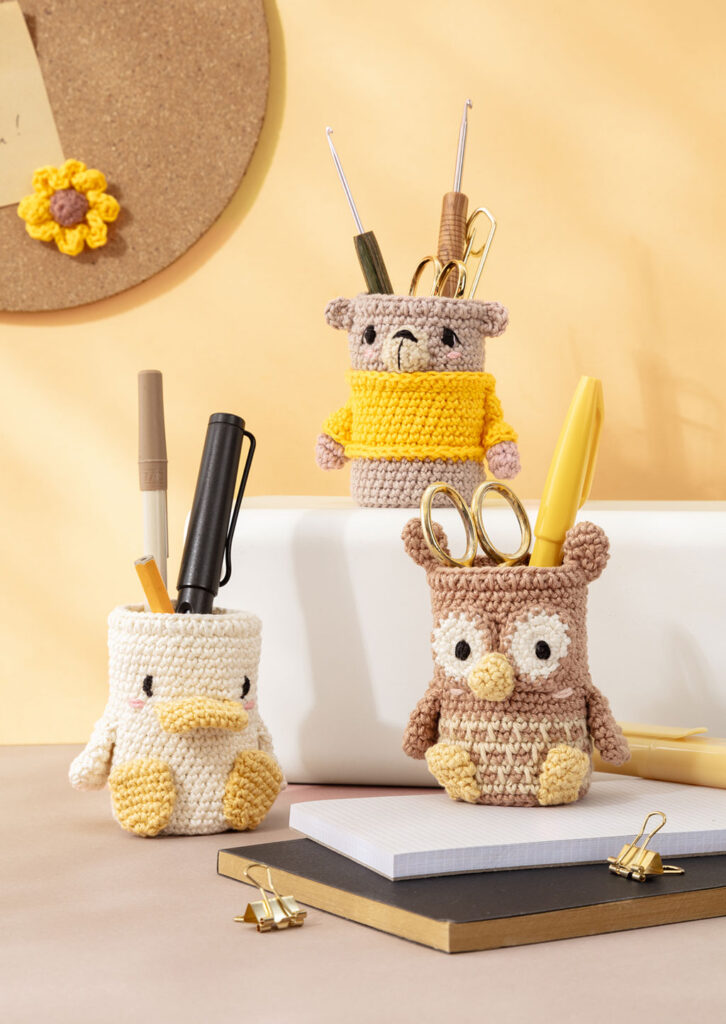 Produktfoto für ein Häkelbuch, das drei gehäkelte Amigurumi-Stiftebecher auf einem Schreibtisch zeigt