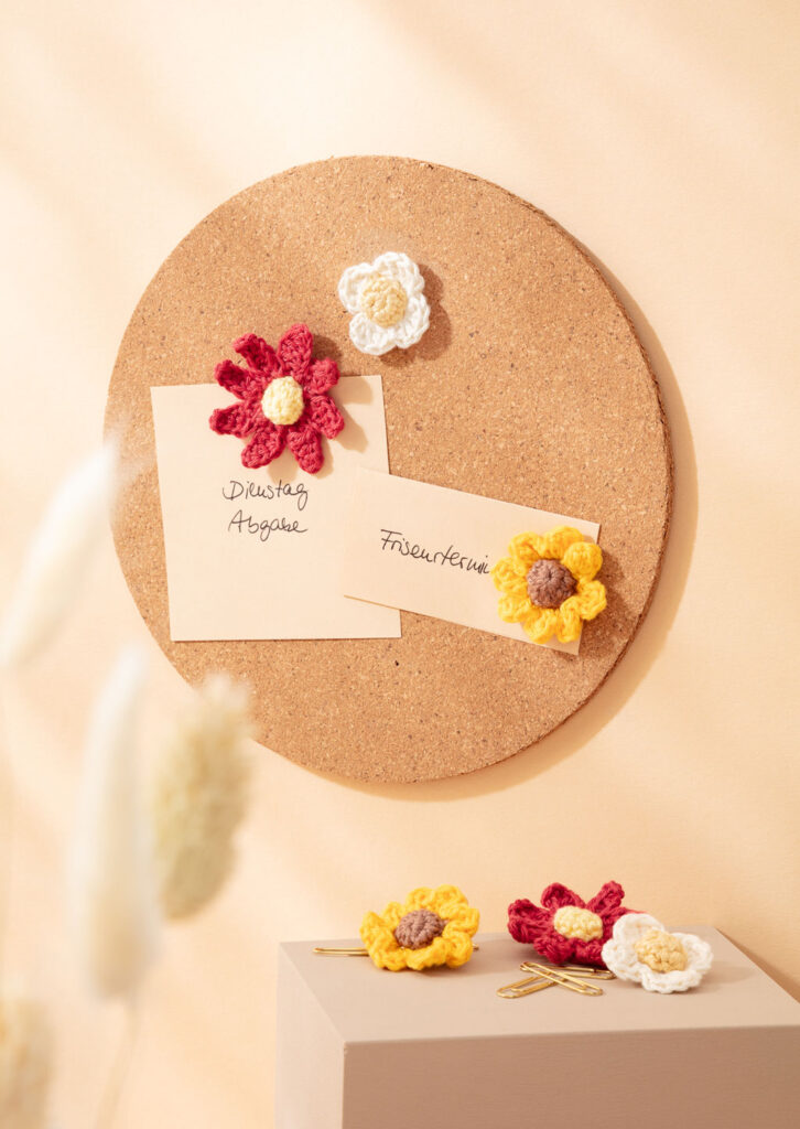 Produktfoto für ein Häkelbuch, das gehäkelte Pins als Blumen an einer Pinnwand zeigt