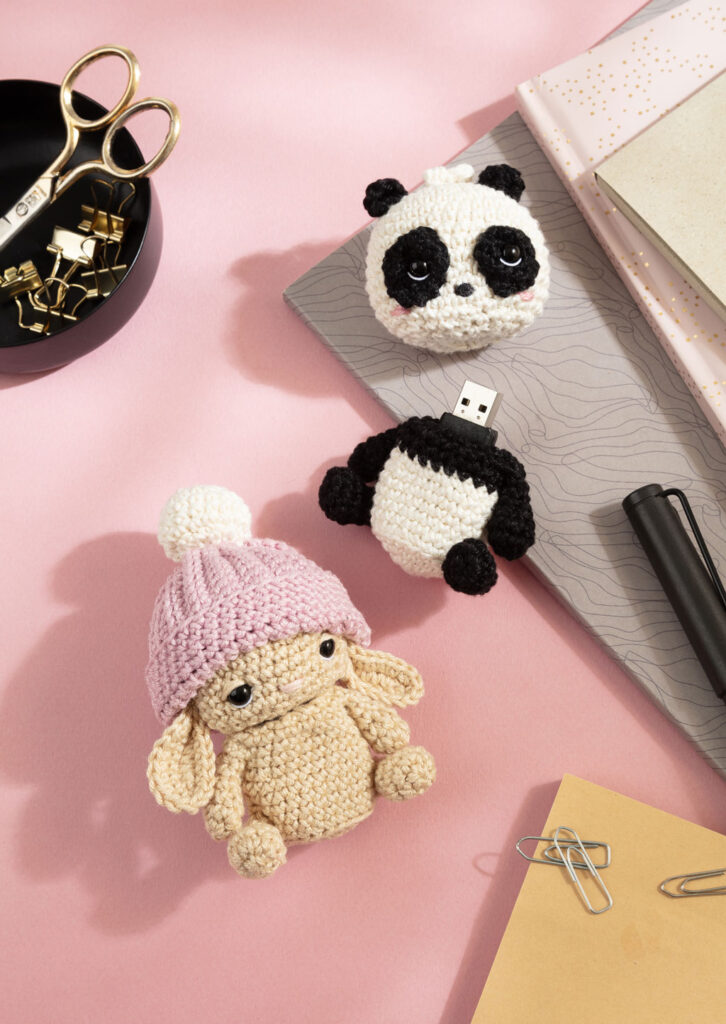 Produktfoto für ein Häkelbuch, das zwei gehäkelte Amigurumi-Tiere als Hülle für den USB-Stick auf einem Schreibtisch zeigt