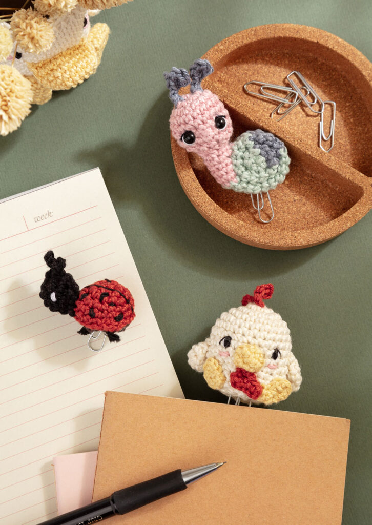 Produktfoto für ein Häkelbuch, das drei gehäkelte Amigurumi-Büroklammern auf einem Schreibtisch zeigt