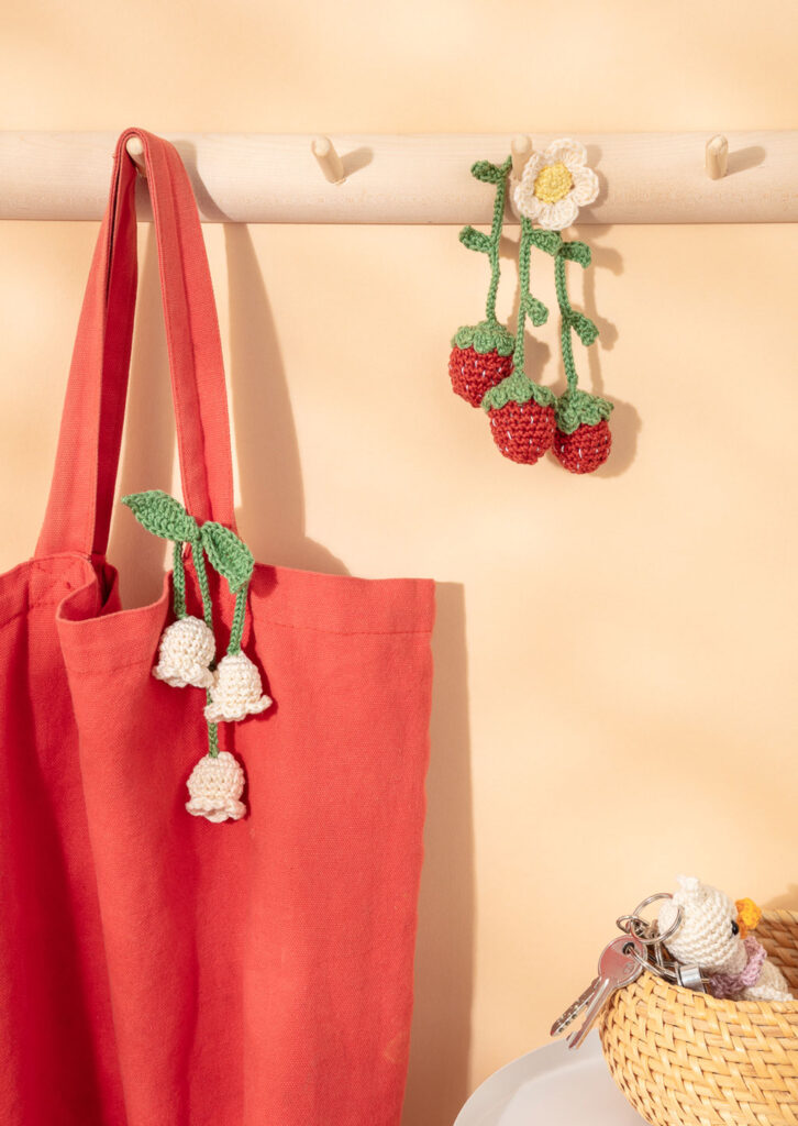 Produktfoto für ein Häkelbuch, das zwei gehäkelte Amigurumi-Taschenbaumler an einem Beutel bzw. an einer Hakenleiste zeigt
