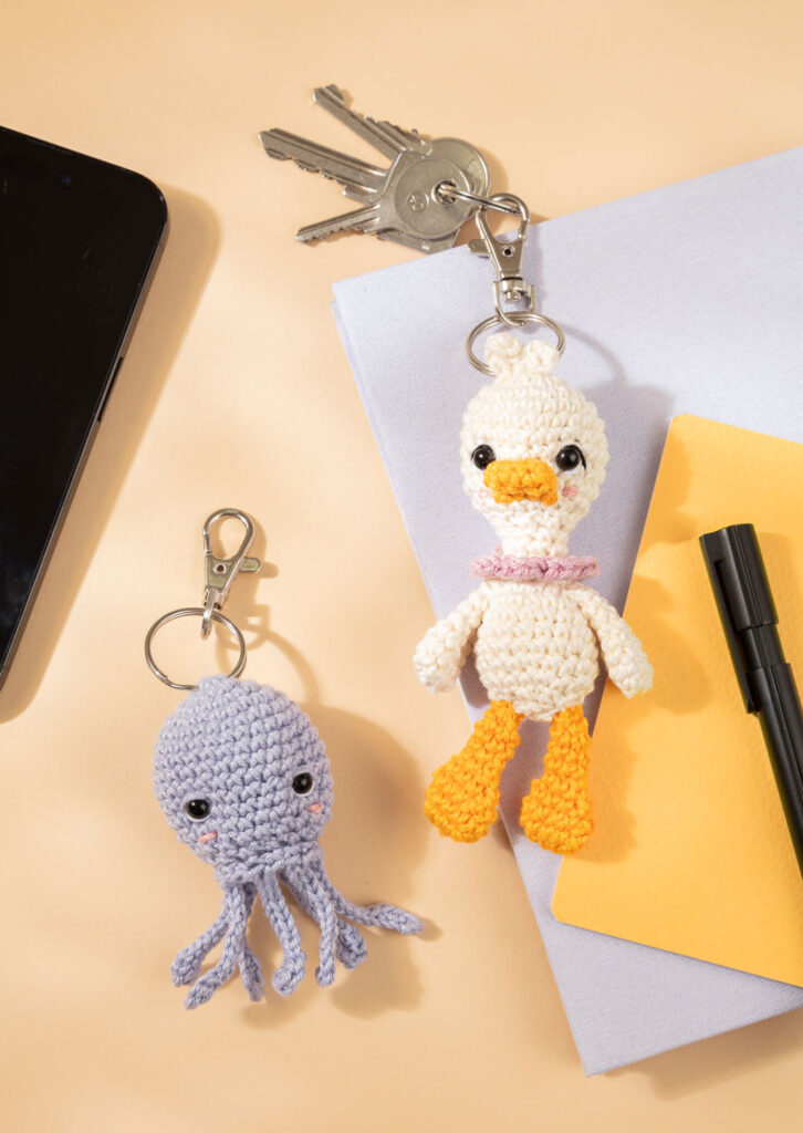 Produktfoto für ein Häkelbuch, das zwei gehäkelte Amigurumi-Schlüsselanhänger auf einem Schreibtisch zeigt