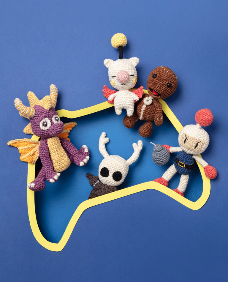 Coverfoto von mehreren Häkelfiguren aus verschiedenen Videospielen arrangiert in einer Kulisse aus einem Papier Cut-Out in Form eines Gaming Controllers