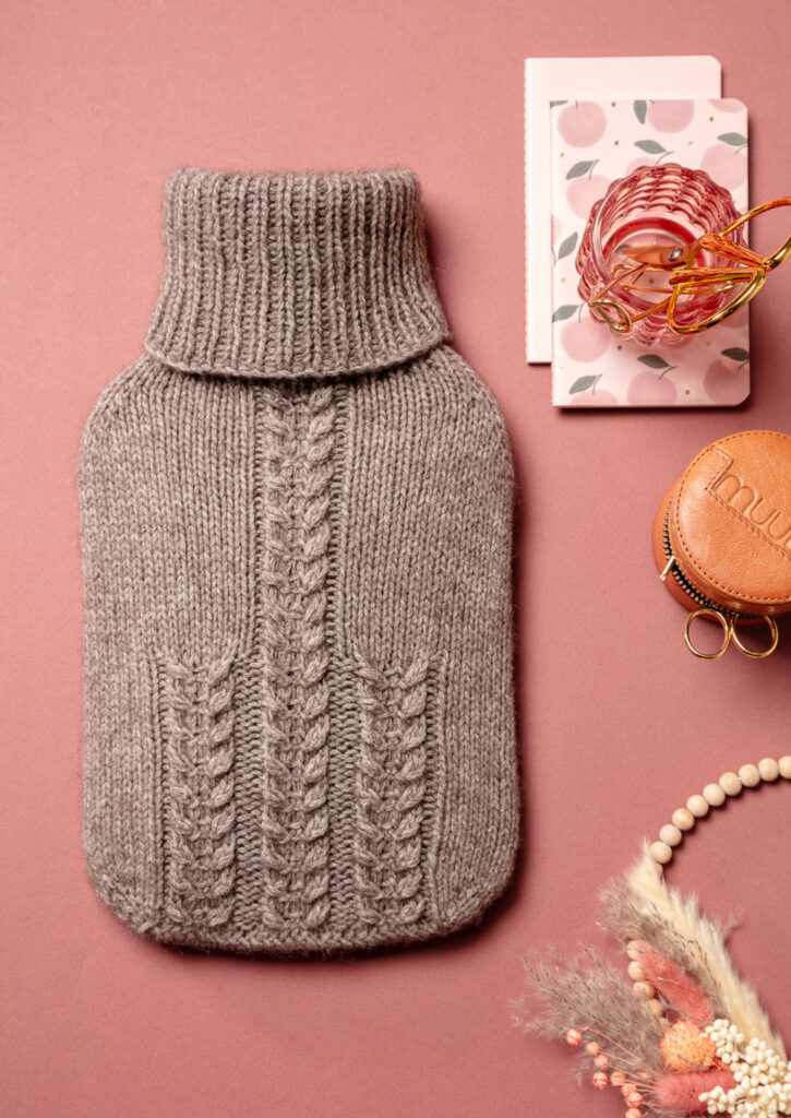 Produktfoto eines gestrickten Wärmflaschenbezugs als Flatlay fotografiert mit romantisch verspielten Deko-Elementen