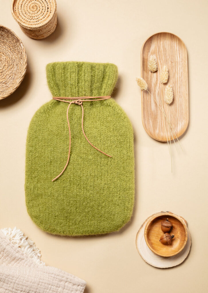 Produktfoto eines gestrickten Wärmflaschenbezugs als Flatlay fotografiert mit warmen, natürlichen Deko-Elementen