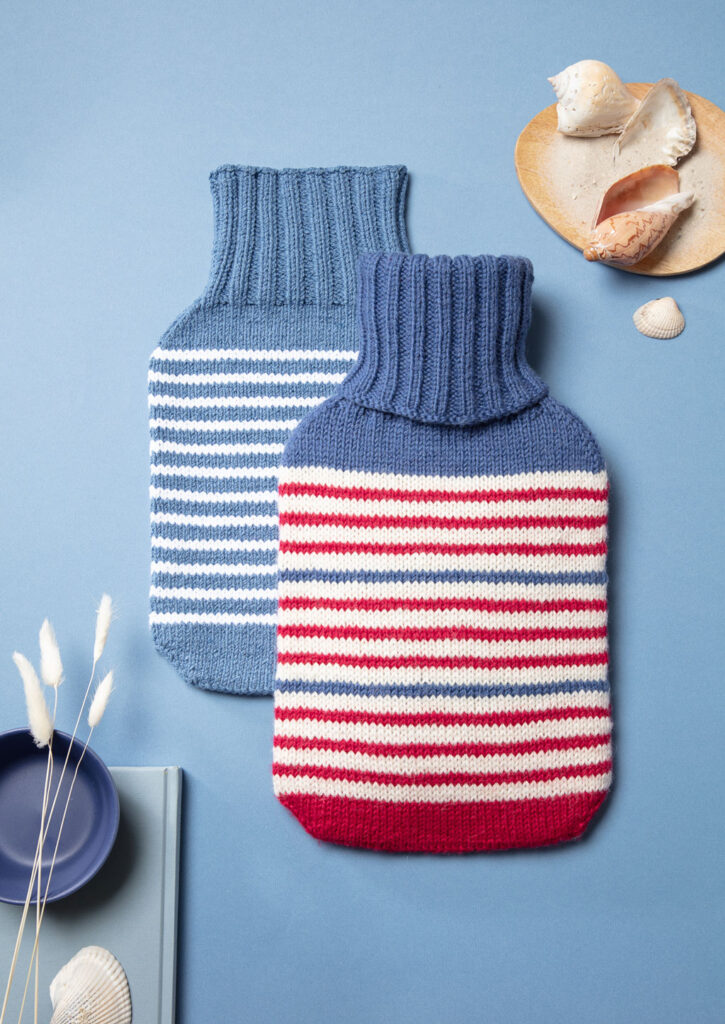 Produktfoto zweier gestrickter Wärmflaschenbezüge mit Streifenmuster als Flatlay fotografiert mit maritimen Deko-Elementen